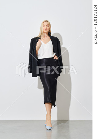 Stylish woman posing in a white blouse, a silk long skirt and a jacket draped over her shoulders Stylish woman posing in a white blouse, a silk long skirt and a jacket draped over her shoulders 120171124