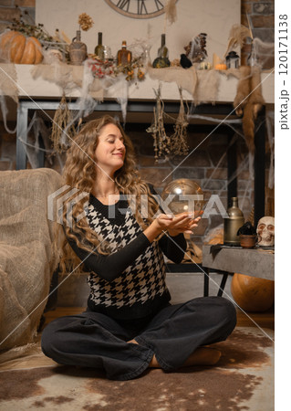 A woman gazes into a crystal ball in a cozy, autumn-themed setting decorated for Halloween 120171138