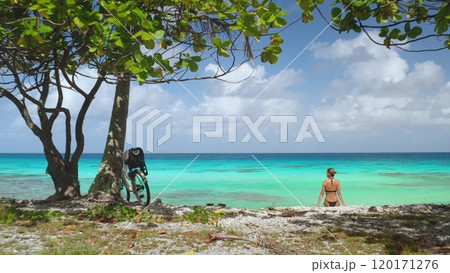 Tourist is enjoying a well-deserved rest on a pristine beach after a bike ride, surrounded by the breathtaking beauty of rangiroa island in french polynesia Tourist is enjoying a well-deserved rest on a pristine beach after a bike ride, surrounded by the breathtaking beauty of rangiroa island in french polynesia 120171276