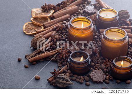 Soy scented candle in a jar. Coffee beans, anise, cinnamon spices. The candles are burning. Dark background. 120171780