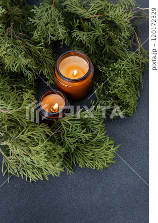 Soy candle in a glass jar. Green thuja branches background. Aromatherapy at home. Scented candles decor 120172329