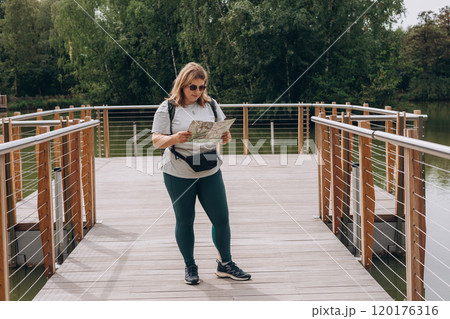 Stylish hipster woman in sunglasses holding paper map, wearing backpack and relaxing in nature. Travel and wanderlust concept. Amazing chill moment, summer time Stylish hipster woman in sunglasses holding paper map, wearing backpack and relaxing in nature. Travel and wanderlust concept. Amazing chill moment, summer time 120176316