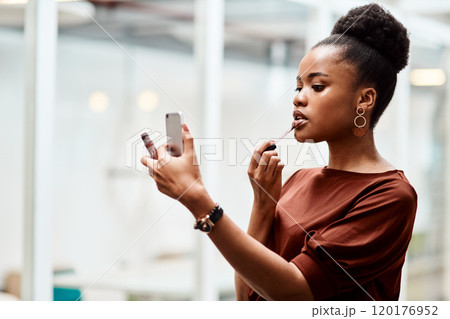Adding a touch of lipstick to complete her boss look. Shot of a young businesswoman applying lipstick while using her cellphone as a mirror in an office. Adding a touch of lipstick to complete her boss look. Shot of a young businesswoman applying lipstick while using her cellphone as a mirror in an office. 120176952