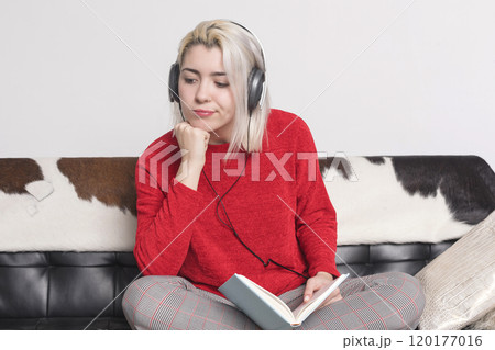 Thoughtful woman with headphones and book sitting on a couch. Thoughtful woman with headphones and book sitting on a couch. 120177016