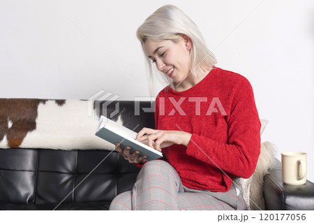 Woman reading a book on a couch, smiling and relaxed. Woman reading a book on a couch, smiling and relaxed. 120177056