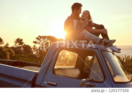 Hilltop romance at sunset. Shot of an affectionate young couple on a roadtrip. 120177169