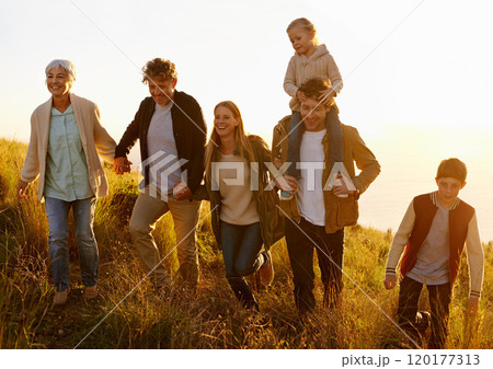 Together every step of the way. A multi-generational family walking up a grassy hill together at sunset. 120177313