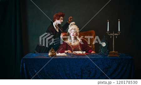 Loyal court servant doing makeup to elderly woman, elegantly dressed empress, in period attire, with serious face, sitting at table with serious face. 120178530