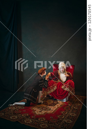 Empress from 18th century offering her hand to her favorite, who kneels in formal gesture of loyalty and kissing hand in respect. Regal and historical charm Empress from 18th century offering her hand to her favorite, who kneels in formal gesture of loyalty and kissing hand in respect. Regal and historical charm 120178545