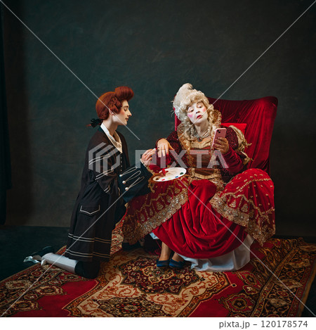 Humorous scene with elderly woman and young man, Medieval empress sitting in chair with young male servant doing painting her nails. 120178574