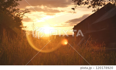 Serene rural sunset scene with a grassy field and barn bathed in warm sunlight 120178920