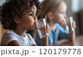 Child drinking water from a glass while sitting 120179778