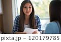 Young woman engaged in conversation holding papers during an interview 120179785