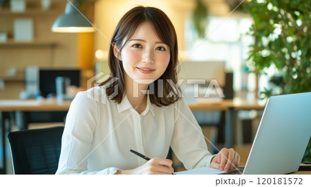 若くてかわいいアジア人女性が、デスクで仕事をしている。笑顔のビジネスシーンの撮影。 120181572