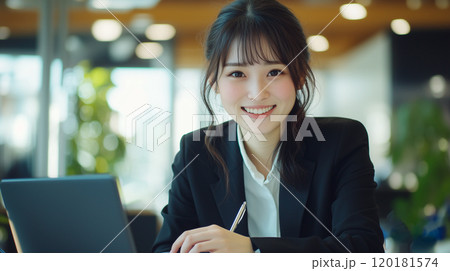 若くてかわいい笑顔のアジア人女性が、スーツを着てデスクで仕事をしている。 120181574