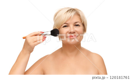 Mature woman holding large makeup brush near her cheek, slightly smiling doing make-up against white studio background. Mature woman holding large makeup brush near her cheek, slightly smiling doing make-up against white studio background. 120181761
