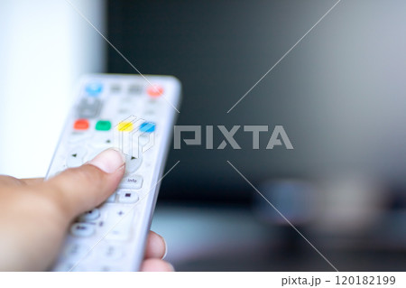 A person is confidently holding a remote control right in front of a tv 120182199