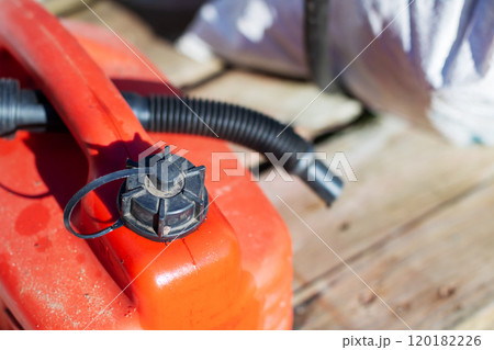 A red gas can sits on a wooden table next to a white bag A red gas can sits on a wooden table next to a white bag 120182226