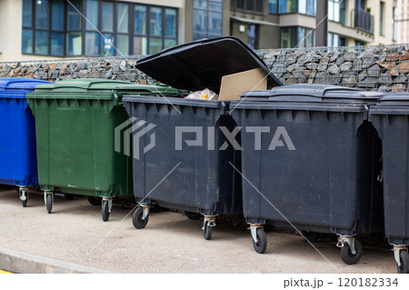 Different colored garbage cans are lined up in front of a building 120182334