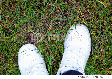 A persons feet are positioned in the grass while wearing white Nike shoes 120182337