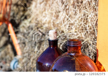 Two brown bottles with corks sit in front of a hay pile 120182373