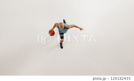 Aerial view of male basketball athlete dribbles basketball preparing for jump against grey studio background. 120182435