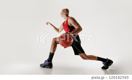 Basketball player in sleeveless shirt and shorts focuses as he dribbles a basketball, ready to make his next move against grey studio background. Basketball player in sleeveless shirt and shorts focuses as he dribbles a basketball, ready to make his next move against grey studio background. 120182593