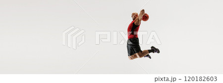 Male athlete dressed in tank top and athletic shorts leaps high, aiming to dunk basketball against grey studio background. Male athlete dressed in tank top and athletic shorts leaps high, aiming to dunk basketball against grey studio background. 120182603