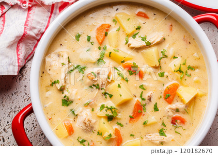 Chicken stew in creamy sauce with potatoes and carrots in red saucepan. Comfort food concept. 120182670