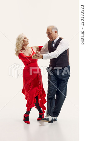 Elderly woman and senior man, elegantly dressed in red dress and black suit, dancing tango with passion isolated on white background Elderly woman and senior man, elegantly dressed in red dress and black suit, dancing tango with passion isolated on white background 120183523
