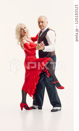 Romantic anniversary. Elderly beautiful woman and handsome man in red dress and black suit, dancing tango isolated on white background 120183525