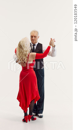 Elegant senior blonde woman in red dress and handsome senior man in black suit dancing tango isolated on white background Elegant senior blonde woman in red dress and handsome senior man in black suit dancing tango isolated on white background 120183549