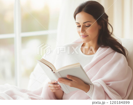 Woman wrapped in a pink blanket reading a book 120184899