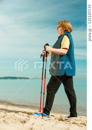 Senior woman practicing nordic walking on beach 120185534
