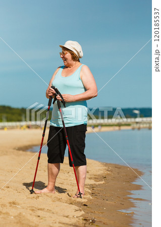 Senior woman practicing nordic walking on beach Senior woman practicing nordic walking on beach 120185537