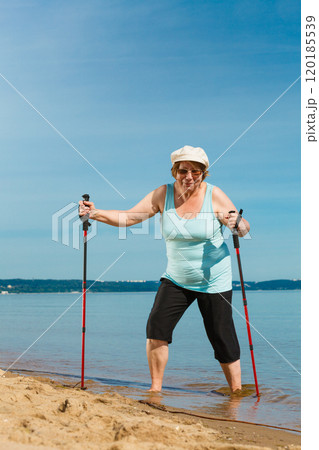 Senior woman practicing nordic walking on beach Senior woman practicing nordic walking on beach 120185539