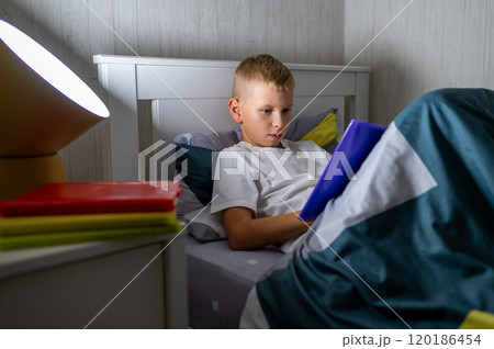 fair-haired teenage boy reading a book before bed 120186454