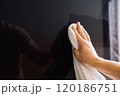 Man wiping dust on plasma panel with white cloth. A hand is seen wiping a glossy black surface with a white cloth, highlighting the effort to maintain cleanliness in a well-lit indoor space. 120186751