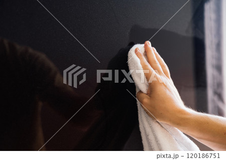 Man wiping dust on plasma panel with white cloth. A hand is seen wiping a glossy black surface with a white cloth, highlighting the effort to maintain cleanliness in a well-lit indoor space. 120186751