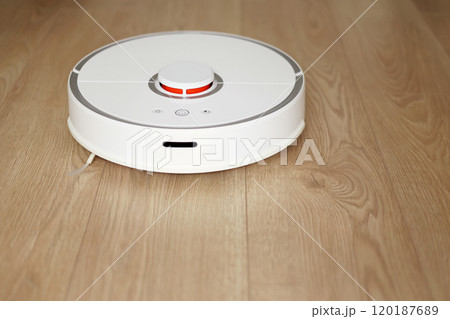 Top view of white wireless autonomous robotic vacuum cleaner on wooden floor. Smart cleaning technology. Self-propelled cleaning robot. Floor cleaning system. Household remote control appliances. Top view of white wireless autonomous robotic vacuum cleaner on wooden floor. Smart cleaning technology. Self-propelled cleaning robot. Floor cleaning system. Household remote control appliances. 120187689