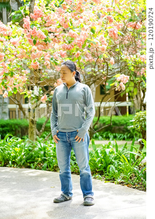 Asian long hair man is wearing a gray long arm T-shirt and standing in front of a lot of flower on the tree in afternoon time. Asian long hair man is wearing a gray long arm T-shirt and standing in front of a lot of flower on the tree in afternoon time. 120190724