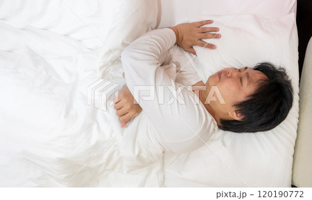 Enjoying a restful sleep, an Asian man finds comfort in his white long-sleeved cotton pajama shirt as he lies on a soft bed, nestled under a gentle blanket and supported by a plush pillow. 120190772