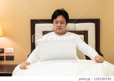 Work from home, a freelancer man leaning against the bed and using his laptop to work online on a bed. Work from home, a freelancer man leaning against the bed and using his laptop to work online on a bed. 120190794