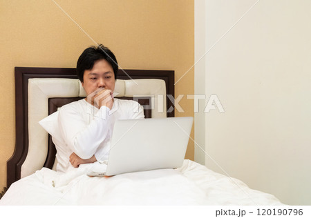 Work from home, a freelancer man leaning against the bed and using his laptop to work online on a bed. Work from home, a freelancer man leaning against the bed and using his laptop to work online on a bed. 120190796