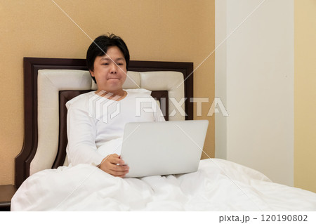 Work from home, a freelancer man leaning against the bed and using his laptop to work online on a bed. Work from home, a freelancer man leaning against the bed and using his laptop to work online on a bed. 120190802