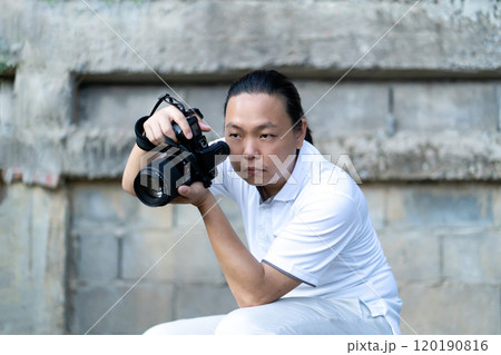 Professional Asian Chinese - Thai Camera man posture and focus in viewfinder and LED screen on mirrorless camera medium format in construction concrete area. Professional Asian Chinese - Thai Camera man posture and focus in viewfinder and LED screen on mirrorless camera medium format in construction concrete area. 120190816