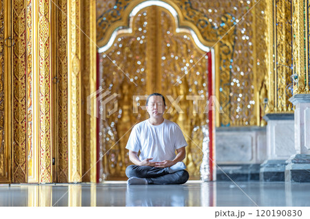 Asian Man meditates on the ground with reflection in the sunlight pouring into the temple church with gold gold Thai pattern blur background. Asian Man meditates on the ground with reflection in the sunlight pouring into the temple church with gold gold Thai pattern blur background. 120190830