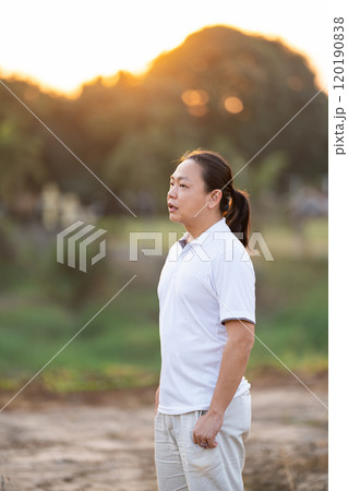 Asian Man long hair stands and relax on the dry field in golden twilight time. Asian Man long hair stands and relax on the dry field in golden twilight time. 120190838