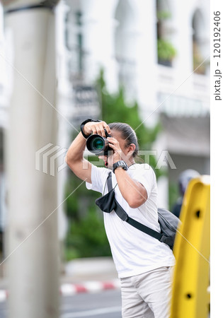 Professional Asian Camera man focus on the image with his mirrorless camera beside the street outdoor field. Professional Asian Camera man focus on the image with his mirrorless camera beside the street outdoor field. 120192406