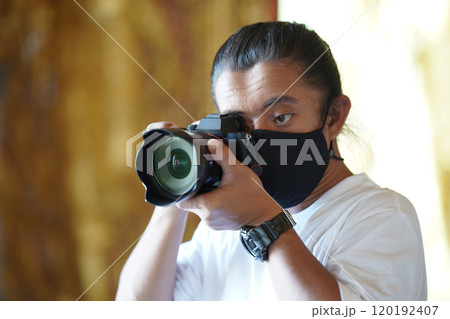 A man wearing black mask is shooting photo through a viewfinder camera with the right eye. A man wearing black mask is shooting photo through a viewfinder camera with the right eye. 120192407